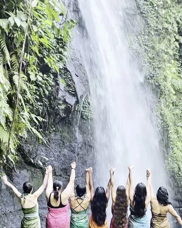The group standing under a waterfall with their arms raised
